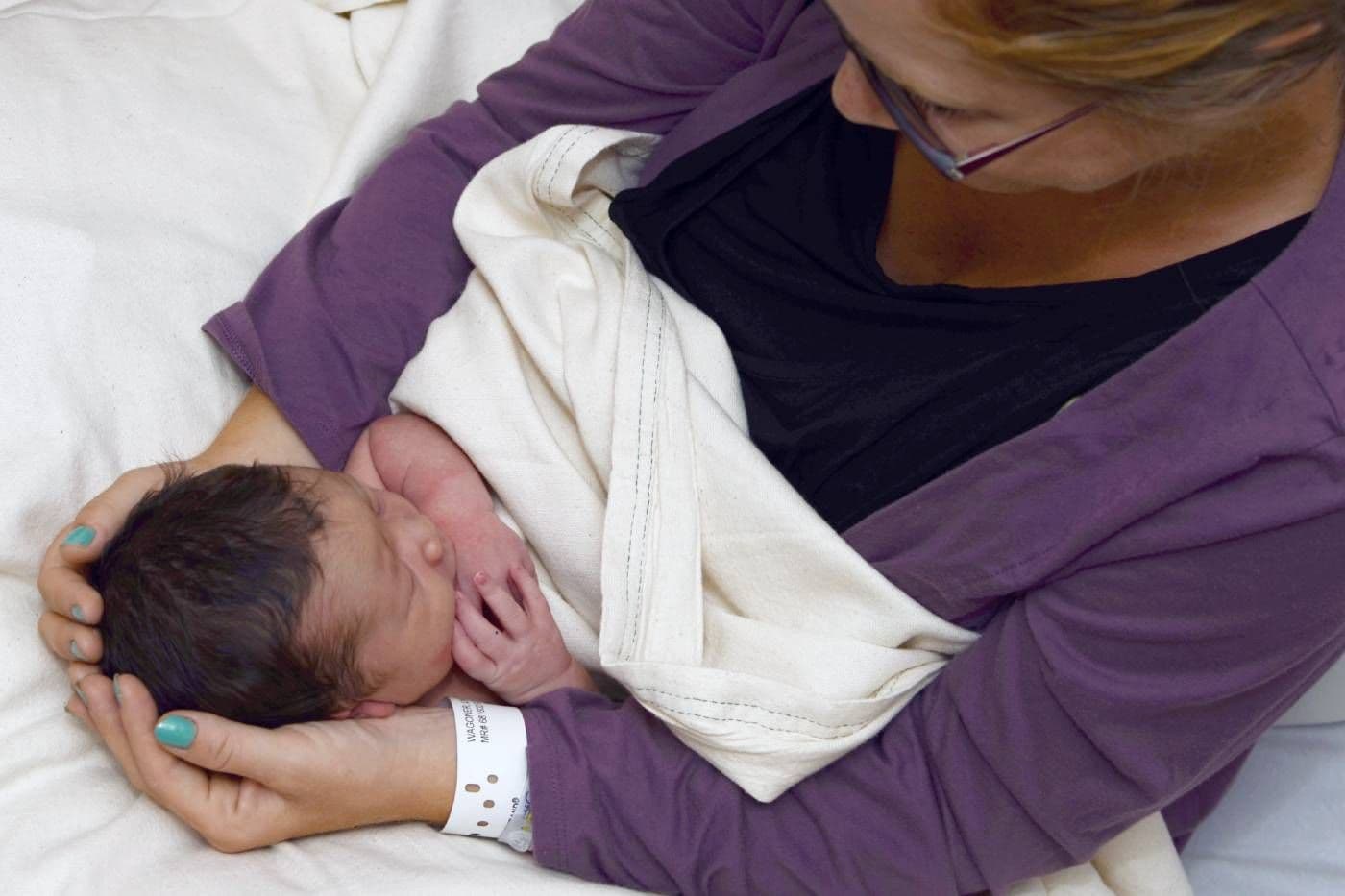 A new mum cradles her newborn baby, who has a full head of hair.