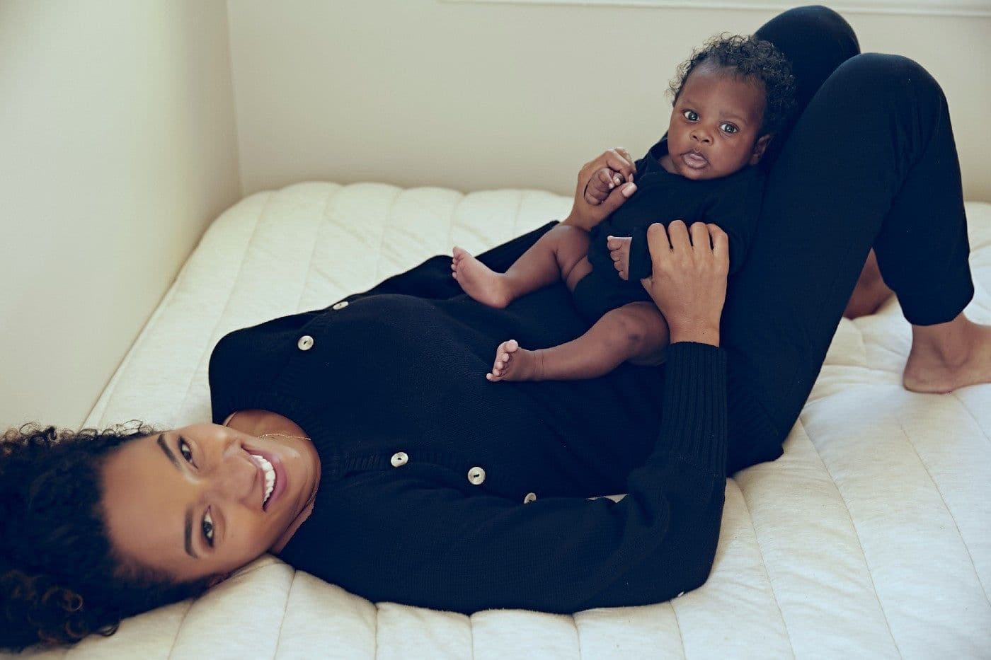Rachel Nicks, founder of Birth Queen, laying on a bed with her infant son.