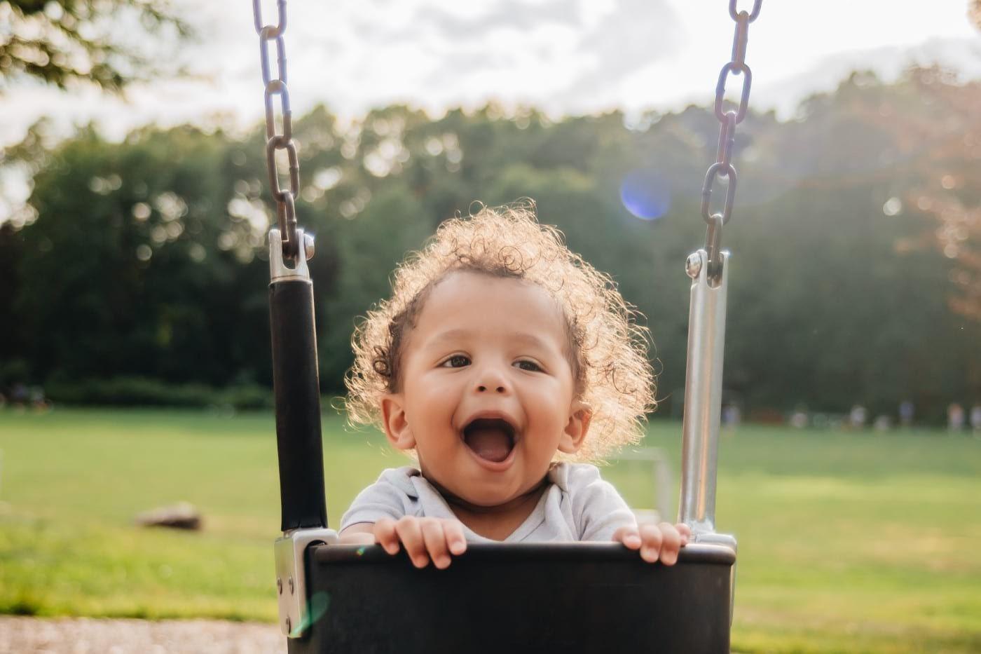 Baby boy laughing while swinging in a baby swing.