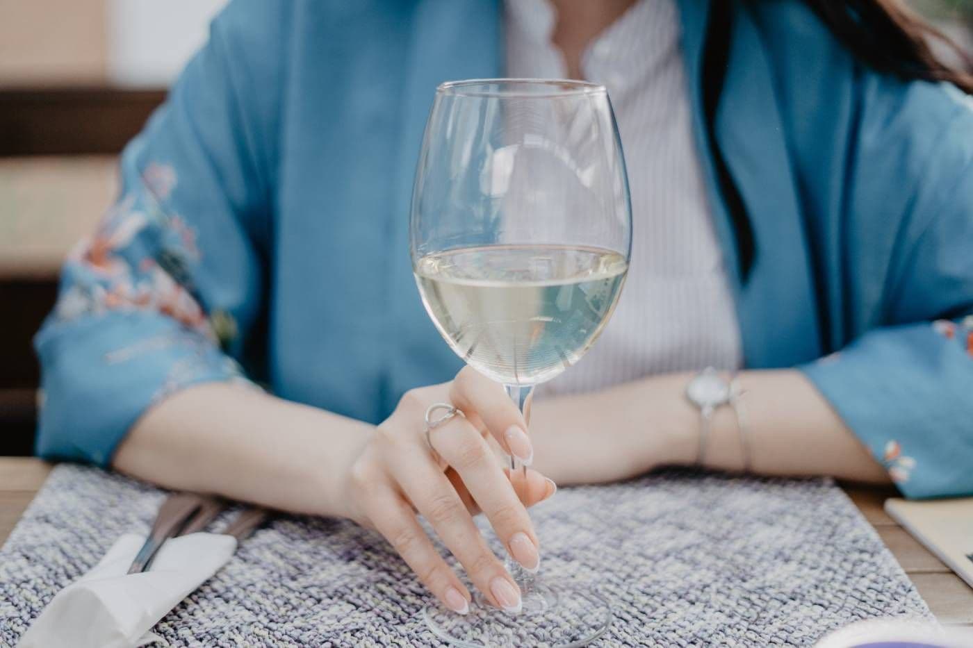 A woman holds a glass of white wine.