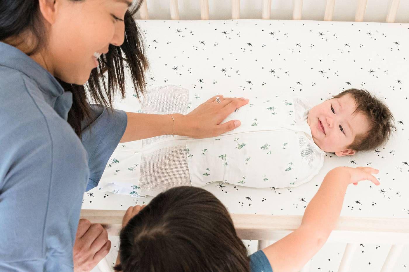 Baby swaddled in Sleepea, mom and big sibling look on