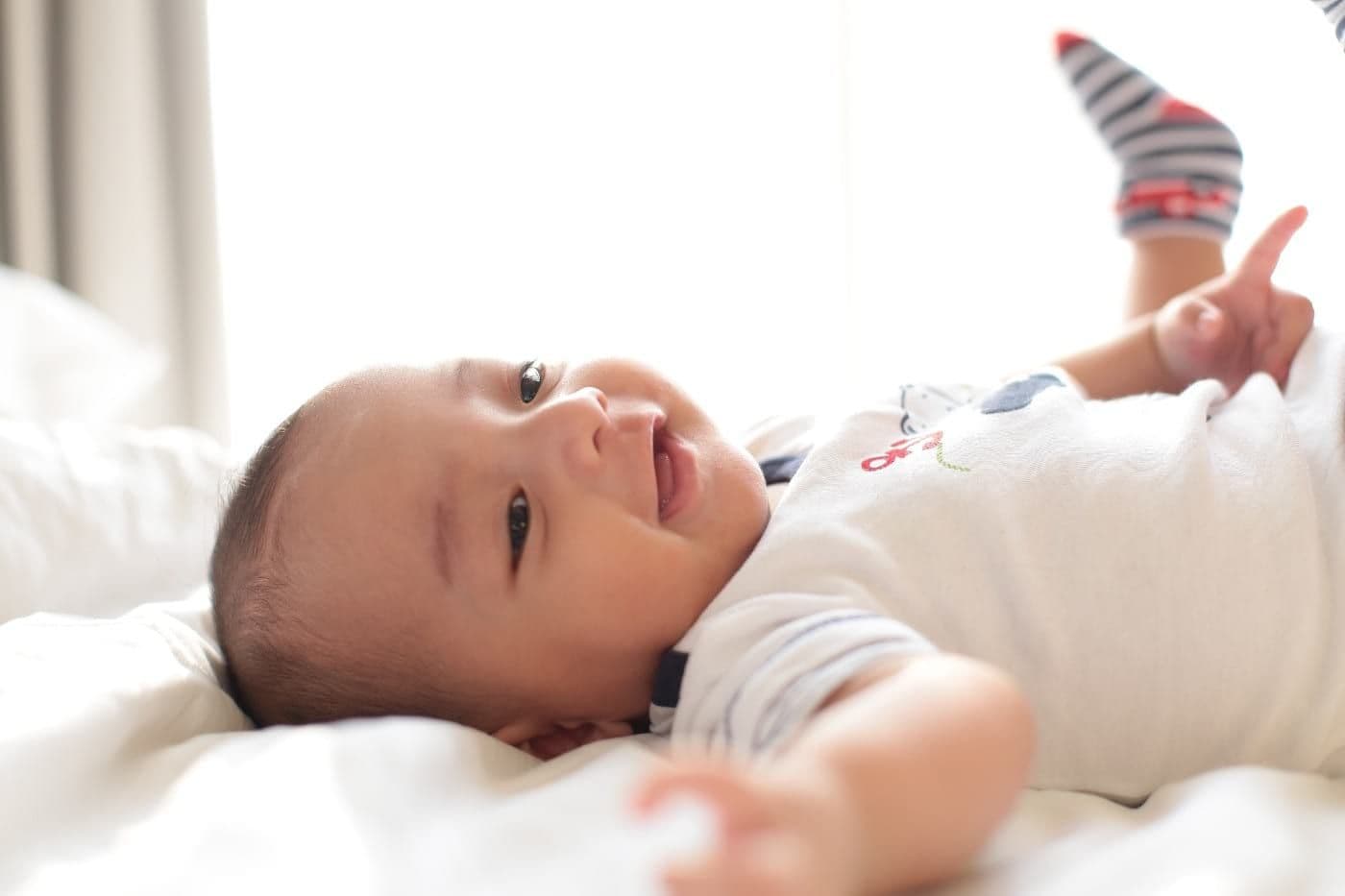 Baby laying on his back on a bed and smiling.