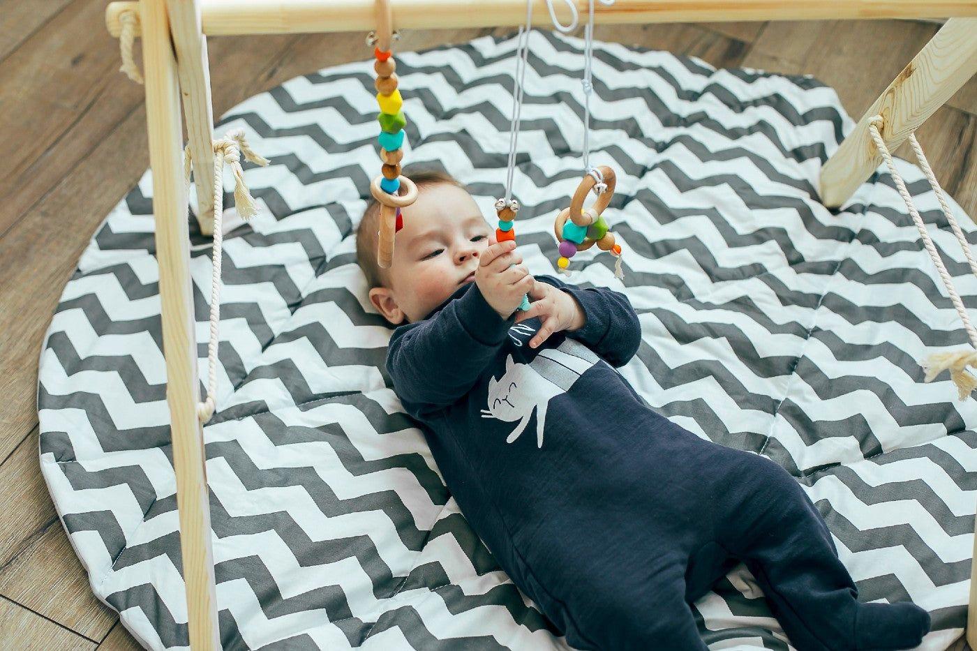 A baby plays under a wooden baby play gym