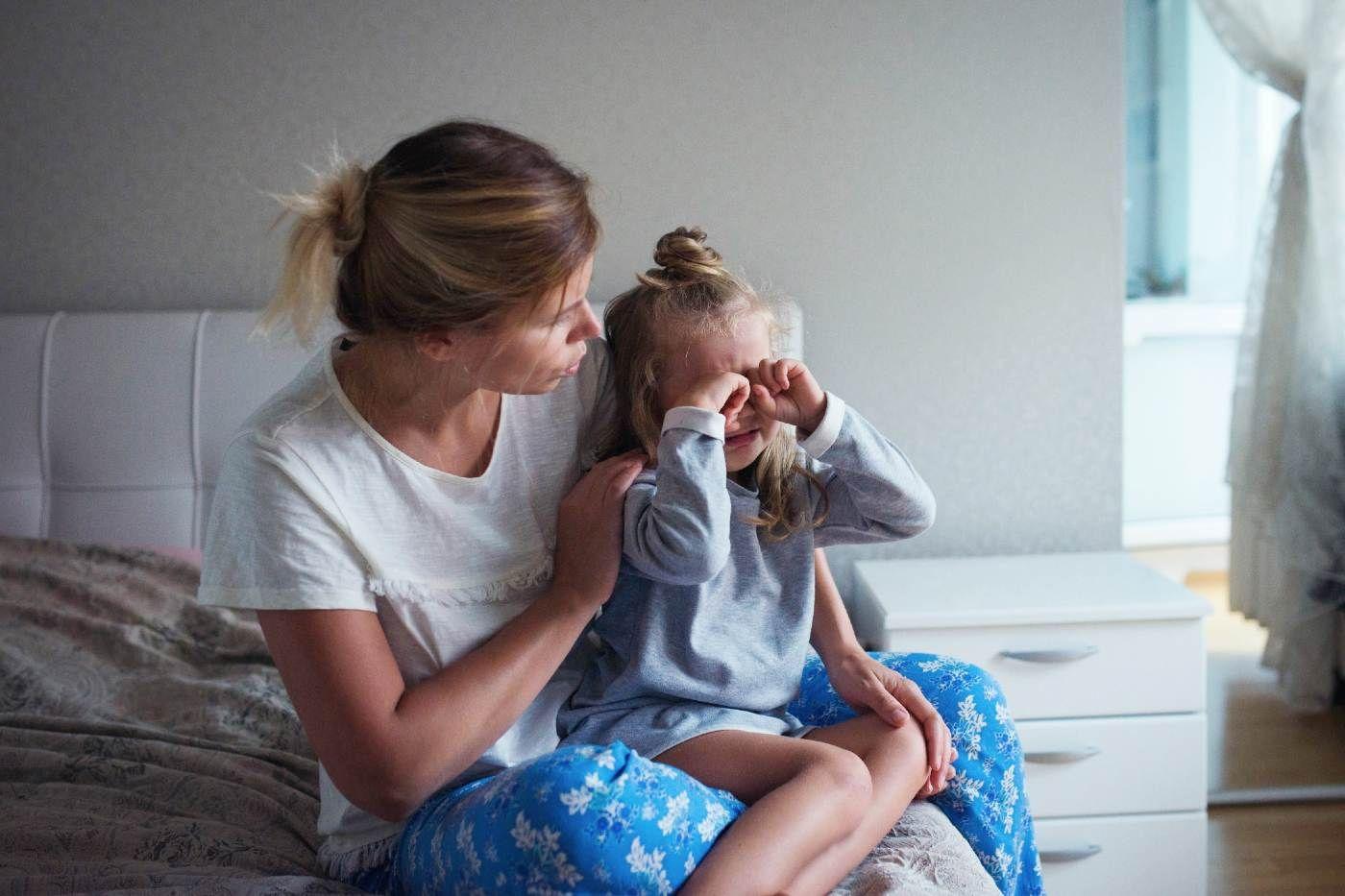 A mother sternly addresses a crying toddler girl on her lap..
