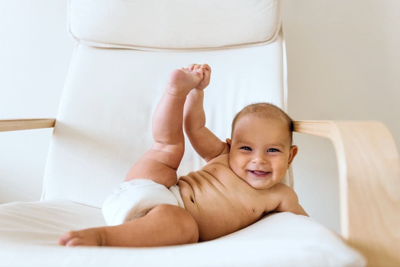Baby reclined on a chair holding onto his toes and smiling.
