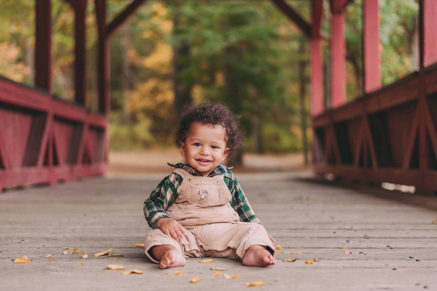 Baby boy sits on a bridge with fall foliage in the background