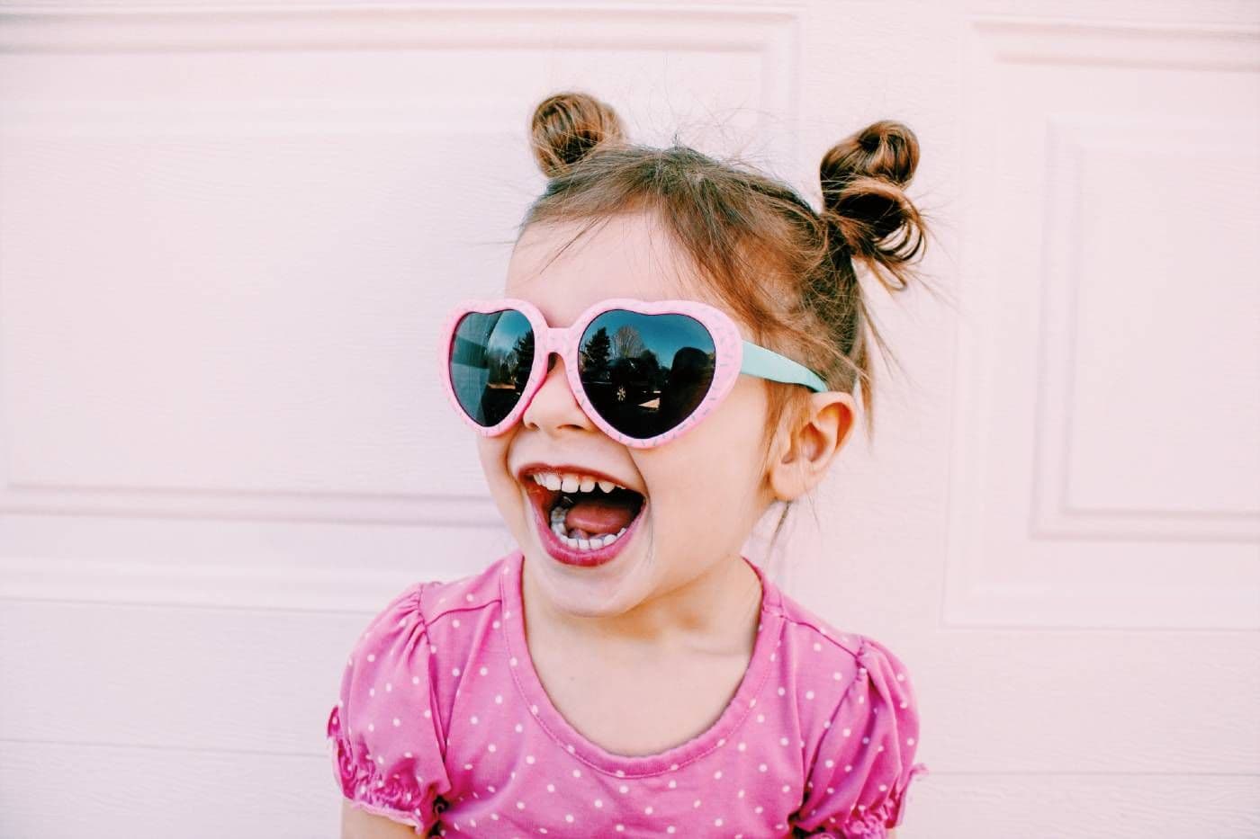 A little girl smiles and wears heart-shaped sunglasses